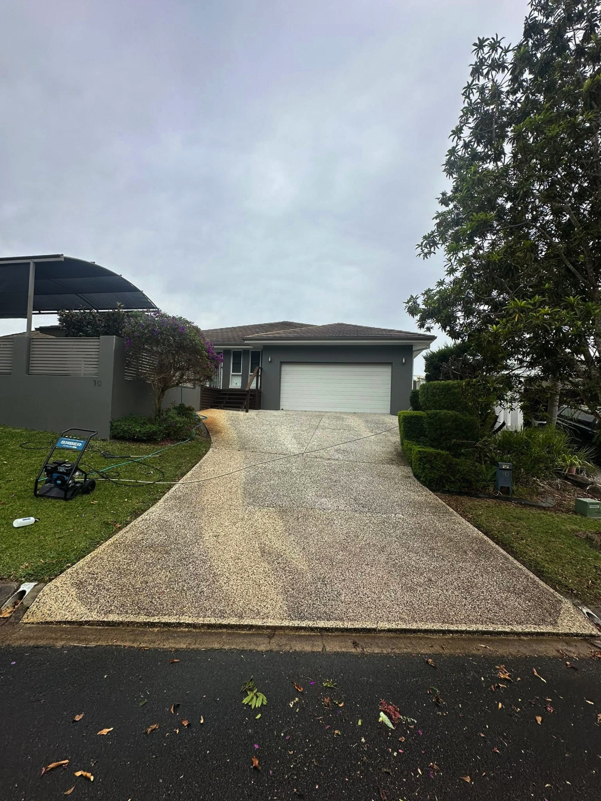 The same driveway before cleaning, grey and stained, with the pressure washer set up on the lawn