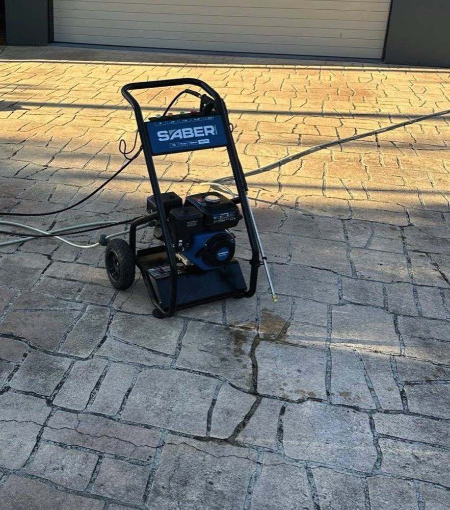 A petrol pressure washer set up on a stamped concrete driveway