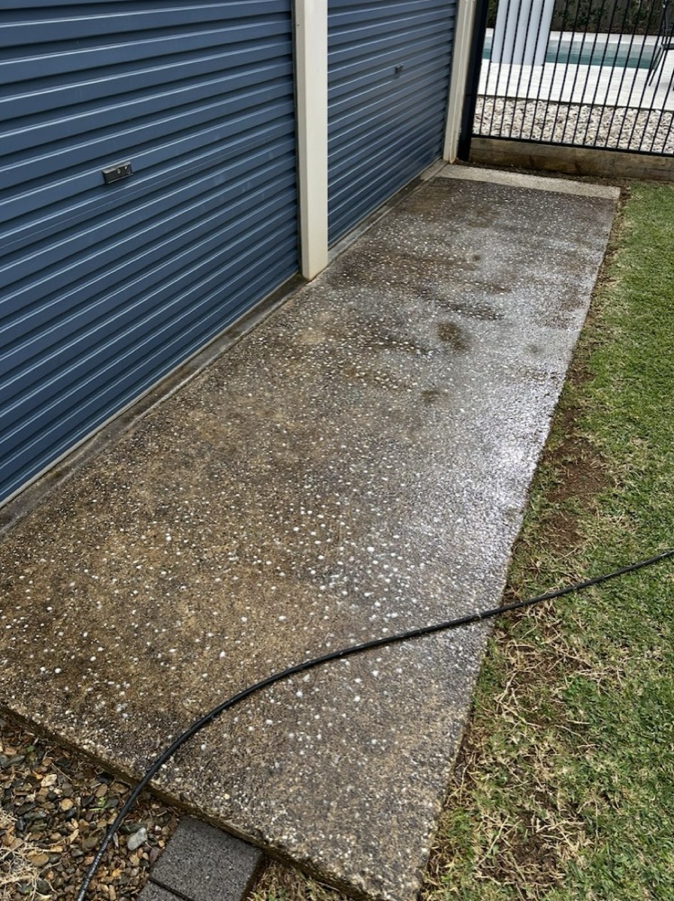 An exposed aggregate slab mid-clean, the washed side reading light and even against the untouched side