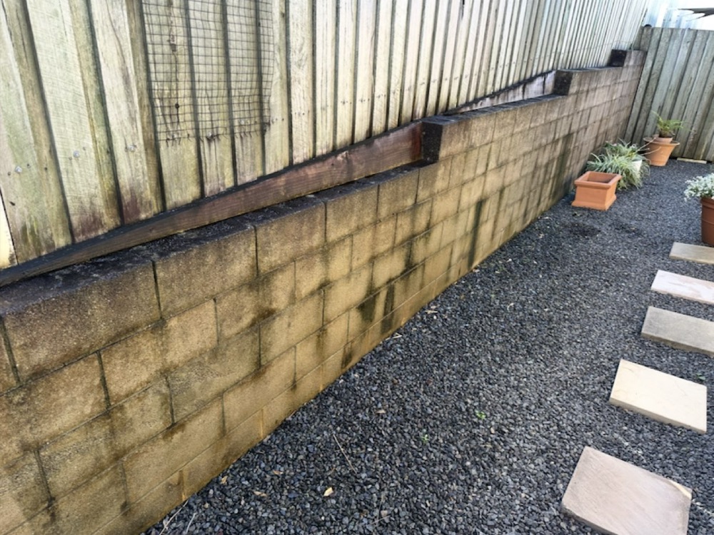 A block retaining wall streaked with mould before pressure washing